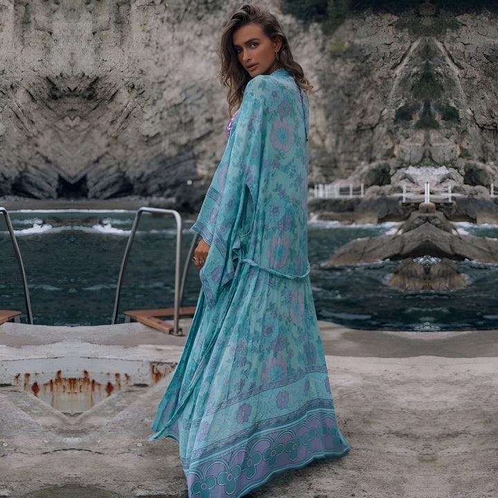 Femme portant un kimono turquoise à motifs floraux près de l'océan. Kimonos élégants pour toutes les occasions. Découvrez notre collection de kimonos uniques.