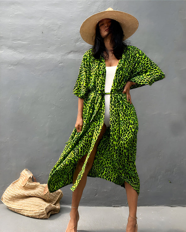 Femme portant un kimono vert à imprimé léopard, un chapeau de paille et un maillot de bain blanc. Kimono de notre collection disponible à l'achat.
