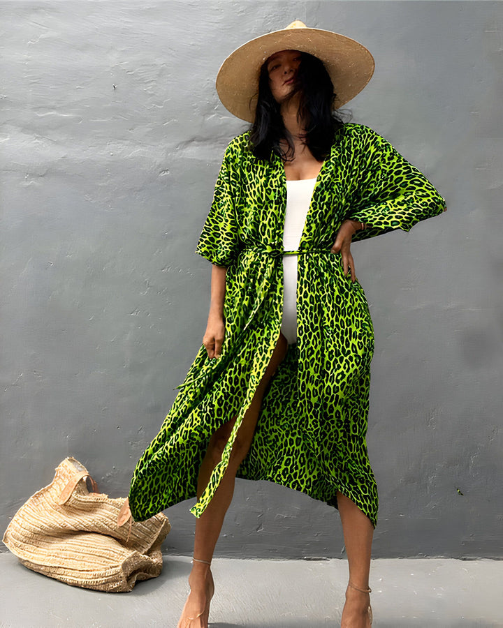 Femme portant un kimono vert à imprimé léopard, un chapeau de paille et un maillot de bain blanc. Kimono de notre collection disponible à l'achat.