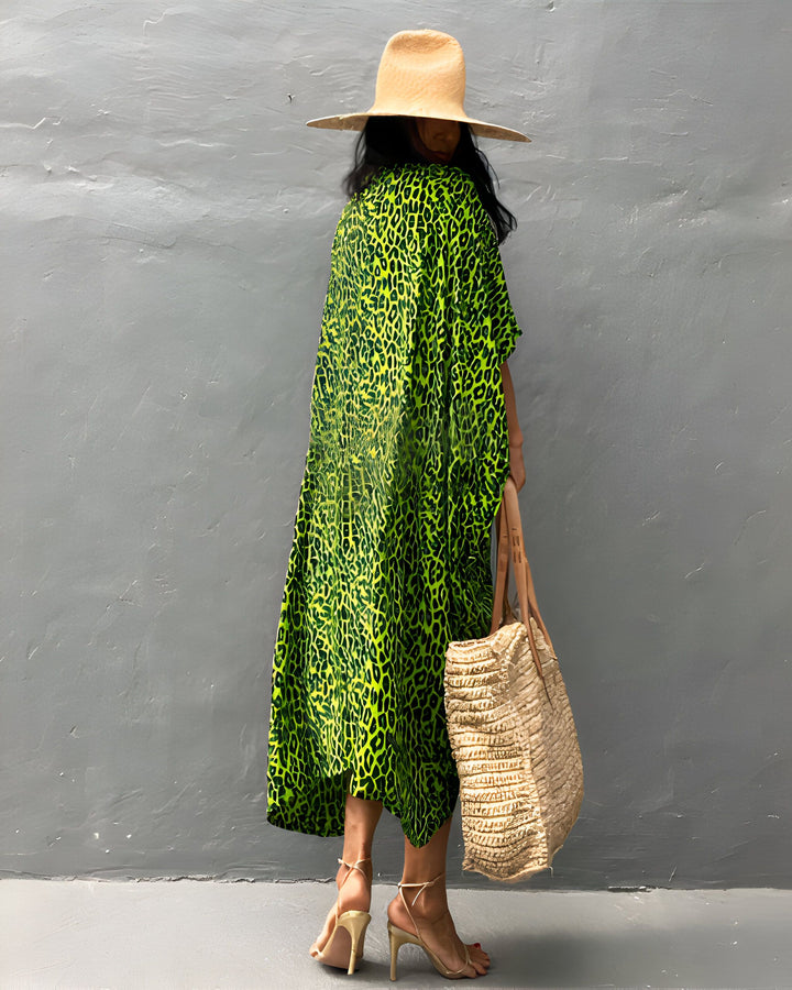 Femme portant un kimono vert à motif léopard, un chapeau de paille et des talons dorés. Elle tient un sac de paille. Découvrez notre collection de kimonos élégants.