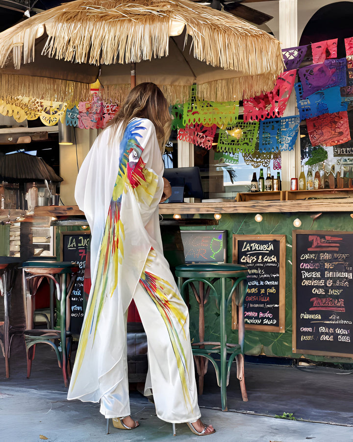 Femme portant un kimono blanc imprimé perroquet devant un bar mexicain. Vêtements de plage, style bohème. Découvrez notre collection de kimonos originaux.