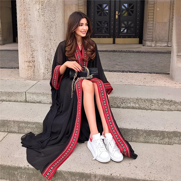Femme élégante assise sur des marches, portant un kimono noir avec des motifs rouges et tenant un petit sac à main noir. Vente de kimonos en ligne.