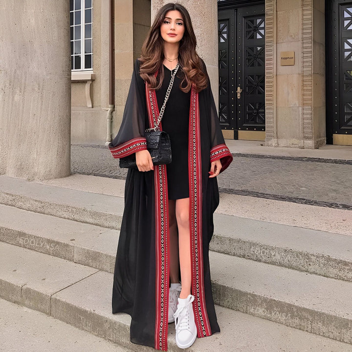Femme portant un kimono noir long avec bordure rouge et motifs, sac à main noir et baskets blanches. Mode kimono, vente de kimonos en ligne.