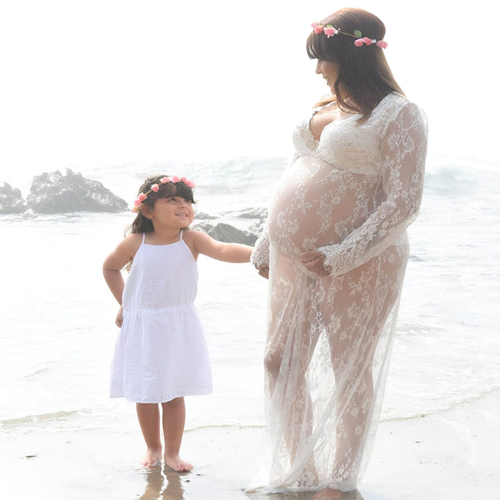Femme enceinte en kimono de dentelle blanche avec sa fille sur une plage, couronnes de fleurs assorties. Kimonos de maternité pour futures mamans et leurs petites filles.