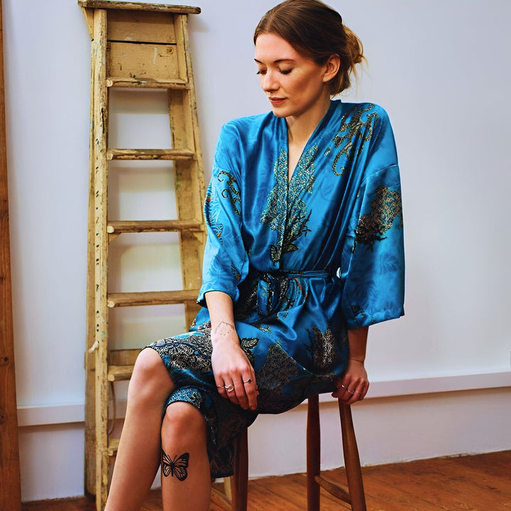 Femme assise portant un kimono bleu à motifs devant une échelle en bois. Kimono en soie disponible à l'achat.