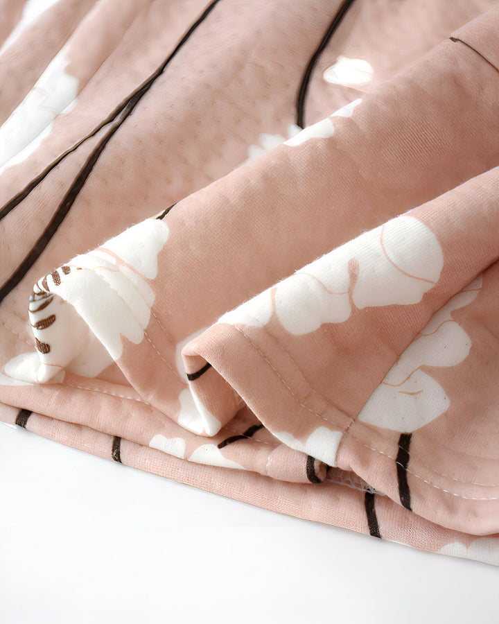 Détail du tissu d'un kimono. Motif floral blanc et brun sur fond rose poudré. Texture douce et plissée, idéale pour nos kimonos de qualité.