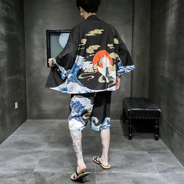 Homme portant un kimono noir et un short assorti, imprimé avec des motifs traditionnels japonais de vagues et de grues devant un soleil rouge. Vêtements de style japonais à la mode.