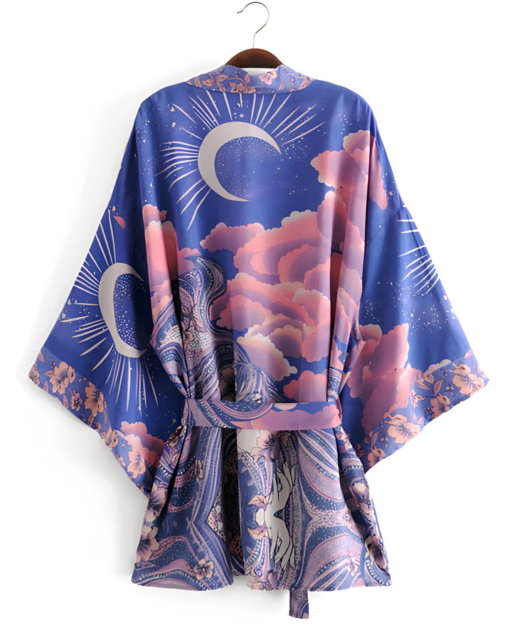 Kimono bleu avec motifs lune, nuages roses et fleurs, suspendu sur un cintre. Vêtement de style japonais, idéal pour ajouter une touche bohème chic à votre garde-robe. Découvrez notre collection de kimonos uniques!