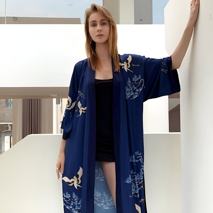 Femme portant un kimono bleu marine avec motifs de grues et de fleurs bleues. Kimono long et fluide, idéal pour la maison ou les sorties. Boutique de kimonos en ligne.