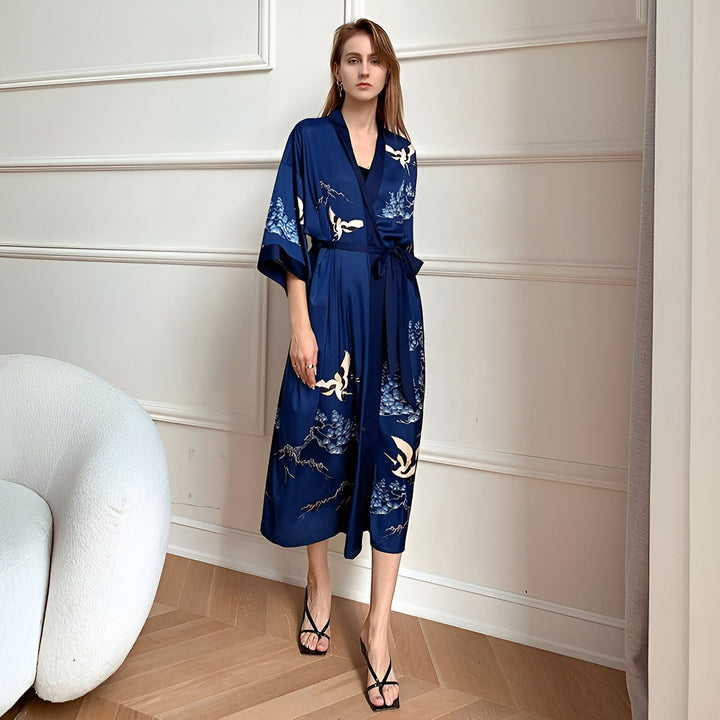 Femme portant un kimono bleu marine en soie avec motifs de grues et de montagnes. Kimono élégant et confortable, idéal pour se détendre à la maison ou pour une soirée spéciale. Disponible dans notre boutique en ligne.
