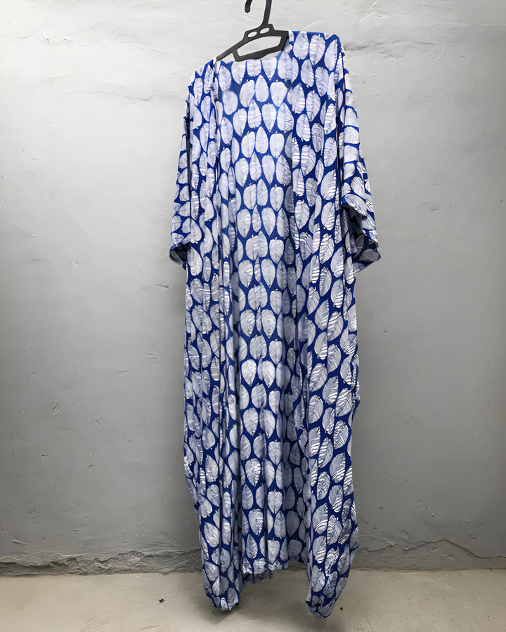 Kimono long bleu à motifs de feuilles blanches suspendu à un cintre. Vêtement ample et léger, idéal pour un look décontracté ou une tenue d'intérieur élégante. Disponible dans notre boutique en ligne de kimonos.