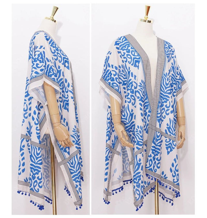 Kimono blanc à motifs bleus sur mannequin, vue de face et de profil. Détails : bordures rayées et pompons bleus. Vêtement idéal pour la plage ou la maison.