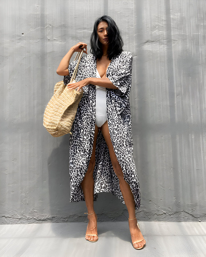 Femme portant un kimono à imprimé léopard, un maillot de bain blanc et un sac de plage. Notre collection de kimonos élégants et confortables.