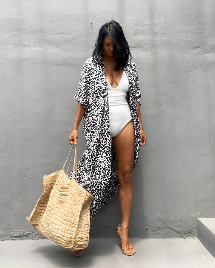 Femme portant un kimono léopard sur un maillot de bain blanc. Sac de plage en paille et sandales à talons dorés. Vêtements de plage, style été, mode féminine. Kimonos disponibles à l'achat.