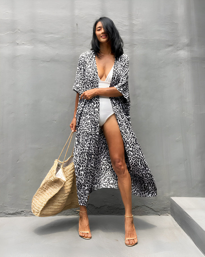 Femme souriante portant un kimono imprimé léopard noir et blanc sur un maillot de bain blanc. Sac de plage et talons hauts. Kimonos élégants à vendre.