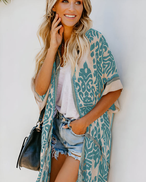 Femme souriante portant un kimono à motifs turquoise et beige, un short en jean et un sac noir. Vente de kimonos pour femmes.