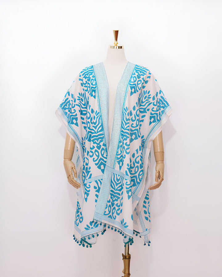 Kimono blanc à motifs bleus orné de pompons, présenté sur un mannequin. Vêtements de plage et d'intérieur.