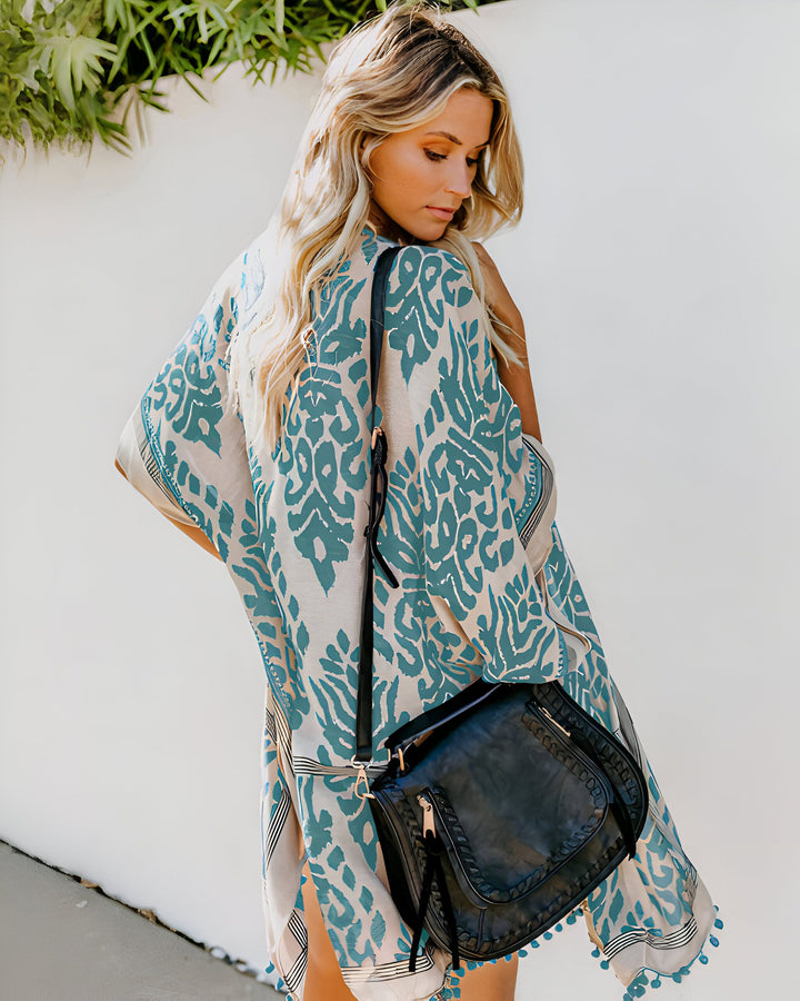 Femme blonde portant un kimono à motifs turquoise et beige avec un sac à bandoulière noir. Vêtements de style kimono à la mode.