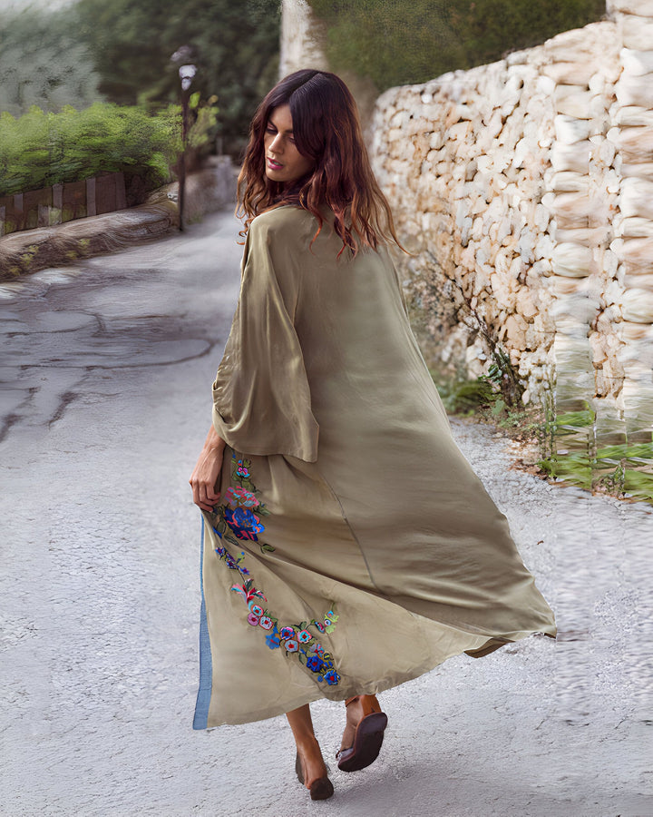 Femme portant un kimono brodé beige. Le kimono a de longues manches amples et des motifs floraux colorés sur le devant. Elle se promène dans une rue pavée. Kimonos à vendre.