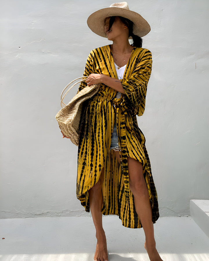 Femme portant une robe longue jaune et noire, chapeau de paille et sac en osier. Style décontracté et estival, mode bohème chic. Idée de tenue pour les vacances.