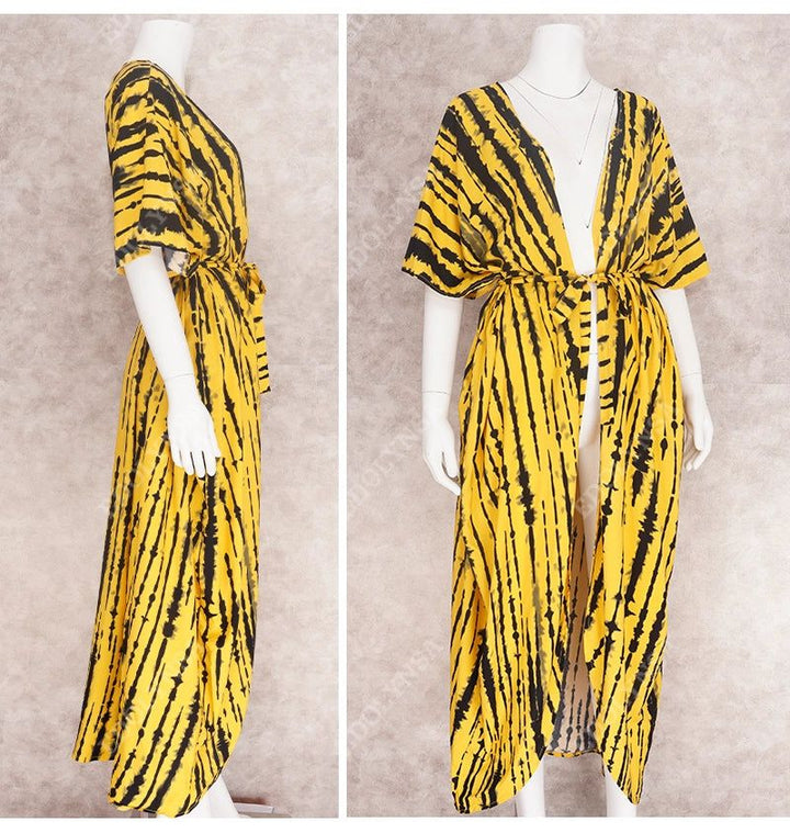 Vue rapprochée d'une robe longue jaune et noire à rayures sur un mannequin, avec une ceinture à nouer à la taille et un décolleté plongeant. La robe a des manches courtes et amples.
