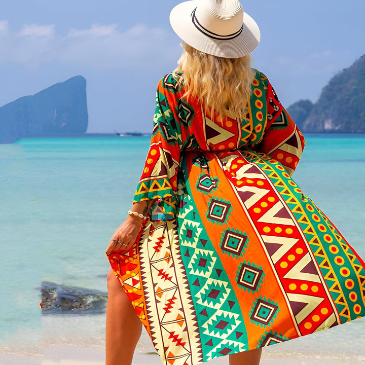 Femme portant un kimono coloré à motifs ethniques sur une plage paradisiaque avec chapeau de paille. Kimonos de plage pour femmes, collection été.