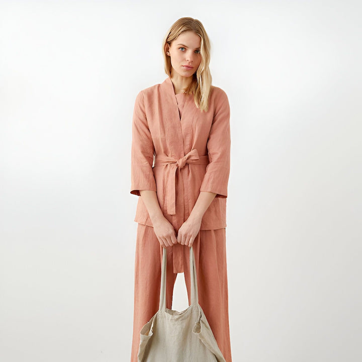 Femme portant un kimono rose avec ceinture assortie, pantalon ample et sac en tissu. Vêtements de style kimono en lin, parfaits pour la détente et un look élégant.