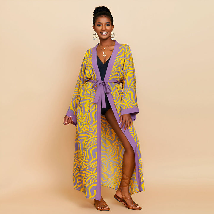 Femme souriante portant un kimono long à motifs zébrés jaunes et violets. Peignoir style kimono, ceinture assortie, idéal pour la maison ou la plage. Vêtements de détente et kimonos disponibles à l'achat.