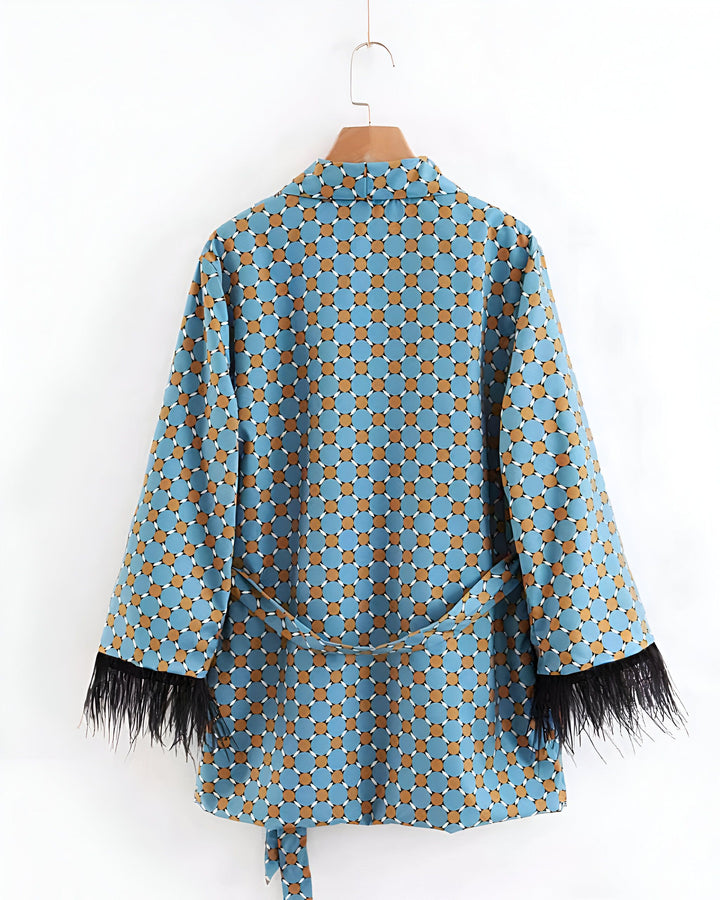 Kimono bleu à motifs géométriques et ceinture, orné de plumes noires aux manches. Vêtement suspendu, vue arrière. Kimono tendance pour femme, collection mode.