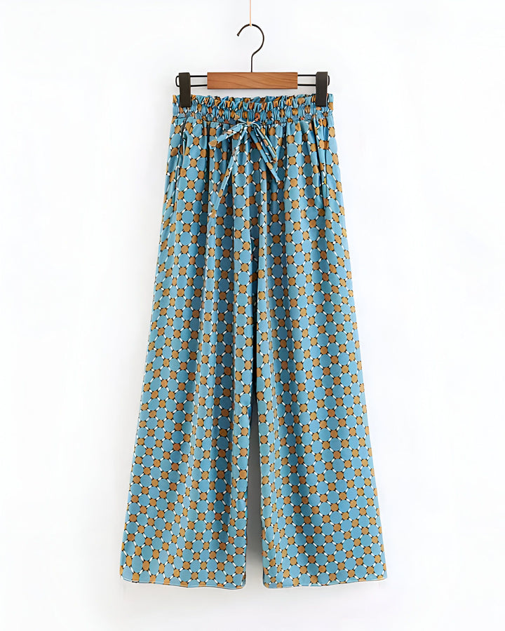 Pantalon large style kimono à motifs géométriques bleus et marrons, suspendu à un cintre. Idéal pour un look confortable et élégant.