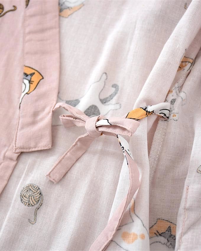 Détail d'un kimono rose clair avec motifs de chats mignons et pelotes de laine. Nœud décoratif rose pâle. Vêtement japonais confortable et stylé.