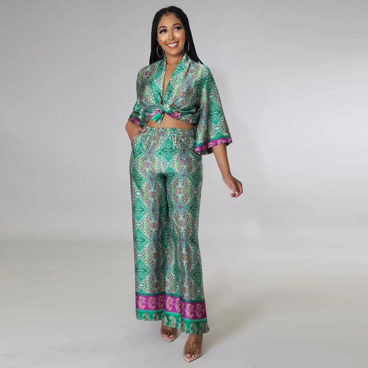 Femme souriante portant un ensemble kimono vert imprimé avec haut noué et pantalon ample. Accessoires : créoles dorées. Vêtements de style kimono à motifs orientaux.