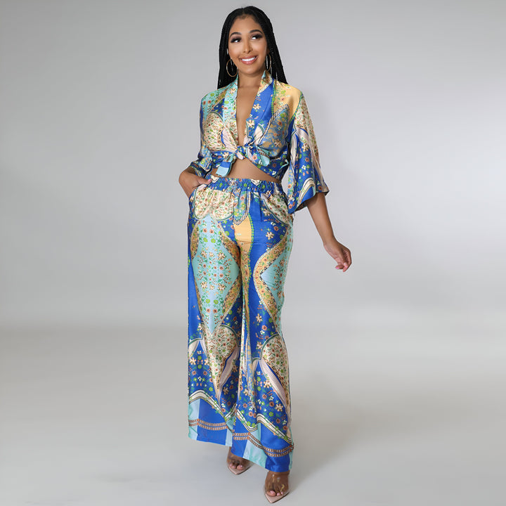 Femme portant un ensemble kimono imprimé bleu et or, haut noué et pantalon ample. Souriante, elle pose avec élégance. Vêtements de style kimono disponibles à l'achat.