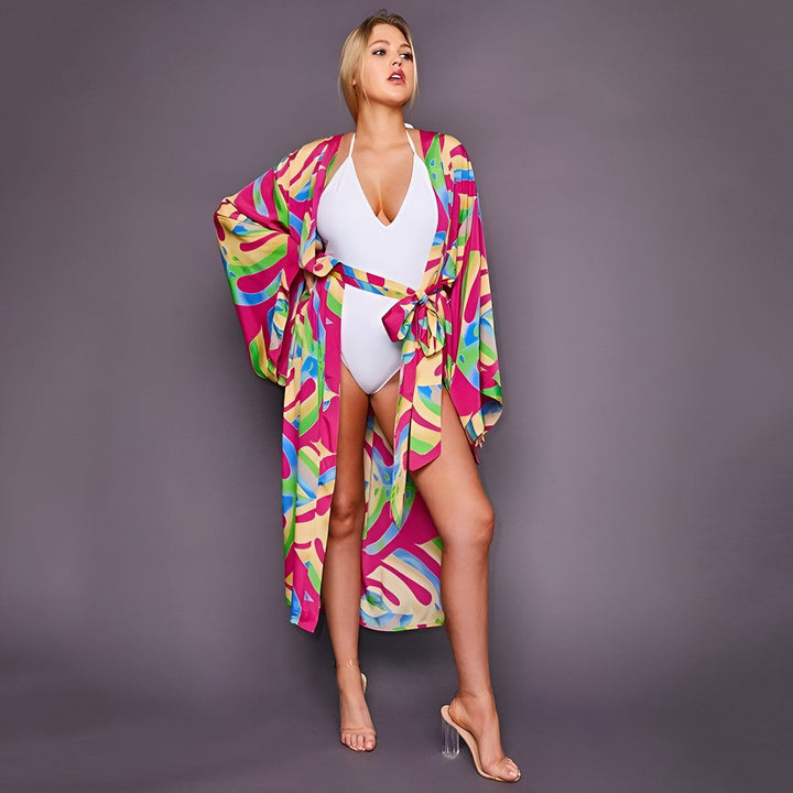 Femme portant un kimono coloré sur un maillot de bain blanc. Kimono à motifs vifs rose, jaune et vert, accessoire de mode estival idéal.