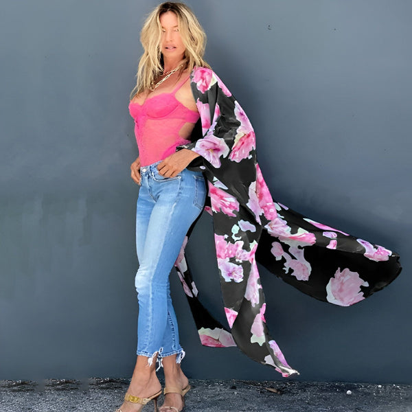 Femme portant un kimono noir à fleurs roses. Kimono long et fluide, porté sur un body rose et un jean. Sandales dorées à talons. Vêtements de style kimono en vente.