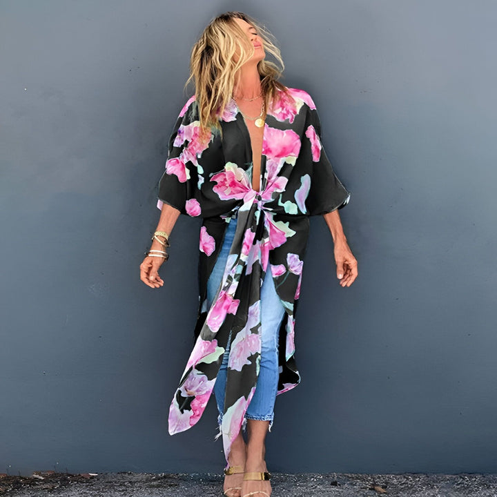 Femme portant un kimono noir à fleurs roses. Vêtement de style japonais, noué à la taille. Idéal pour un look décontracté et élégant. Découvrez notre collection de kimonos.