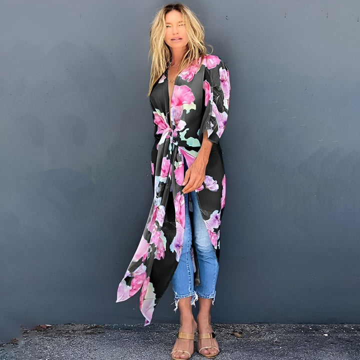 Femme portant un kimono long à fleurs roses et noires, noué à la taille. Tendance mode kimono pour toutes les occasions. Découvrez notre collection de kimonos élégants.