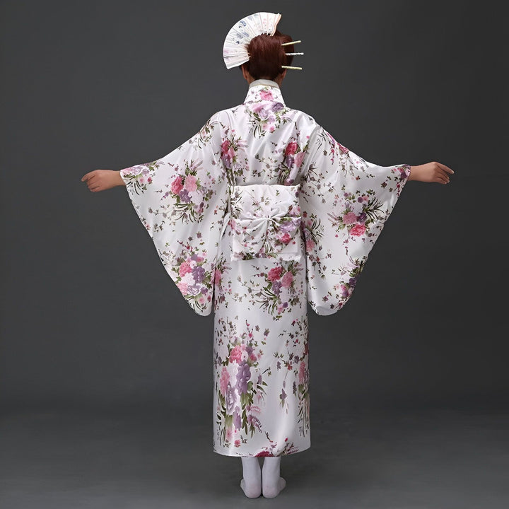 Femme portant un kimono blanc à motifs floraux, vue de dos. Kimono traditionnel japonais, disponible à l'achat. Accessoires inclus : obi et éventail.