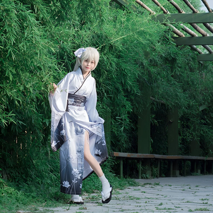 Jeune femme en kimono floral blanc et noir, pose devant un fond de verdure luxuriante. Vente de kimonos authentiques et modernes. Découvrez notre collection unique de kimonos japonais.