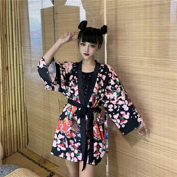Femme portant un kimono noir à motifs floraux roses et blancs, noué à la taille par une ceinture noire. Kimono tendance disponible à l'achat.