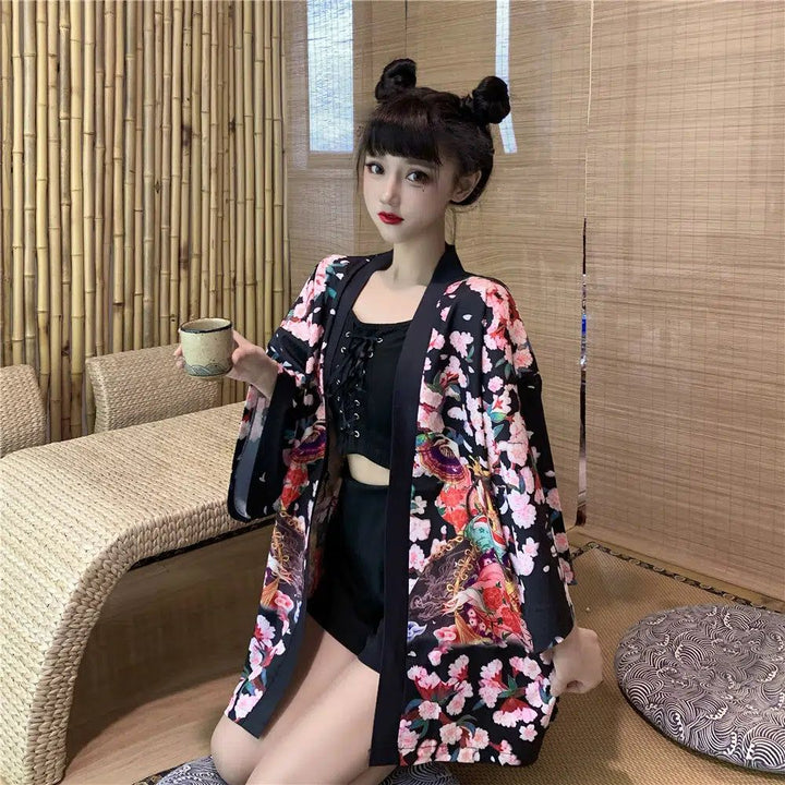 Femme portant un kimono fleuri noir et rose, tenant une tasse. Kimono de style japonais à fleurs, disponible à l'achat. Mode kimono pour femmes.