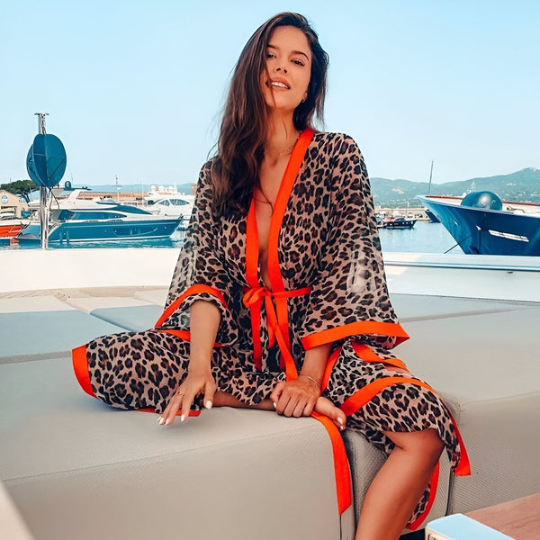 Femme souriante assise sur un yacht, portant un kimono imprimé léopard avec bordures orange. Kimono tendance, vêtement d'été, style vacances. Collection de kimonos imprimés.