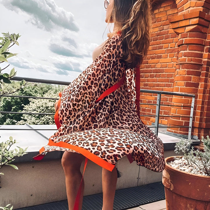 Femme portant un kimono à motif léopard avec garniture orange vif. Vente de kimonos en ligne. Mode féminine, vêtements d'extérieur. Vue depuis un balcon ensoleillé.