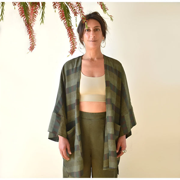 Femme portant un kimono à carreaux vert et marron. Vêtement ample et confortable, idéal pour se détendre avec style. Découvrez notre collection de kimonos uniques.