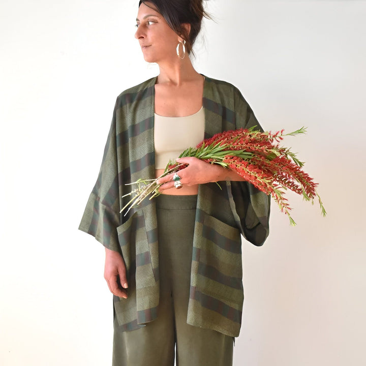Femme portant un kimono à rayures vertes et marron, tenant des fleurs rouges. Vêtements kimono tendance pour femmes. Boutique en ligne de kimonos.