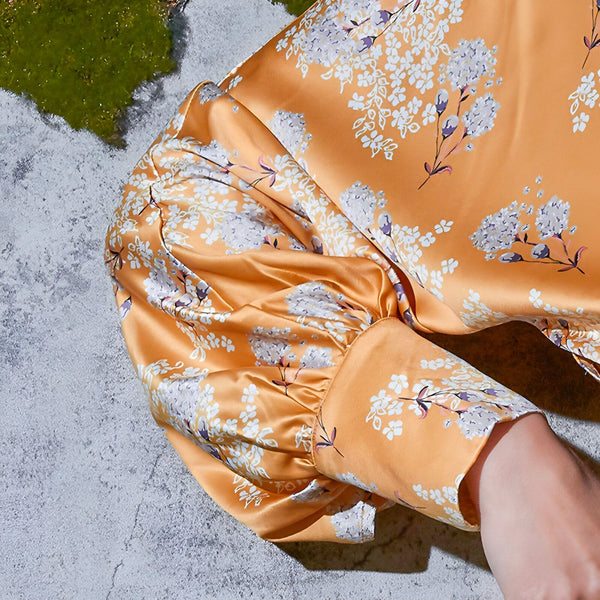 Détail d'un kimono orange à motifs floraux blancs. Manche bouffante en soie. Vêtement japonais élégant pour femme, disponible dans notre collection.