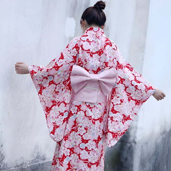 Femme portant un kimono rouge à fleurs avec un grand nœud rose dans le dos. Kimonos japonais traditionnels à vendre.