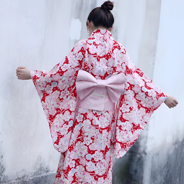 Femme portant un kimono rouge à fleurs avec un grand nœud rose dans le dos. Kimonos japonais traditionnels à vendre.