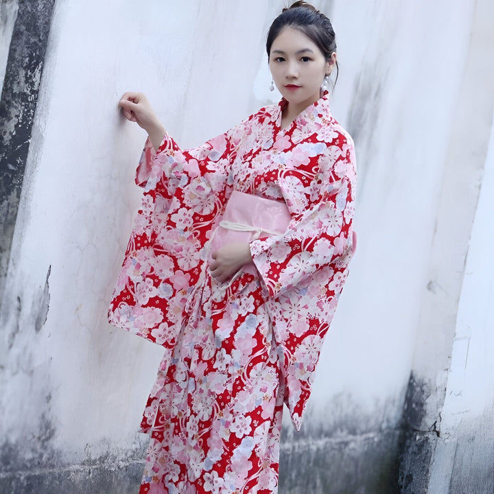 Femme portant un kimono rouge à motifs floraux, obi rose. Vêtements traditionnels japonais à vendre.