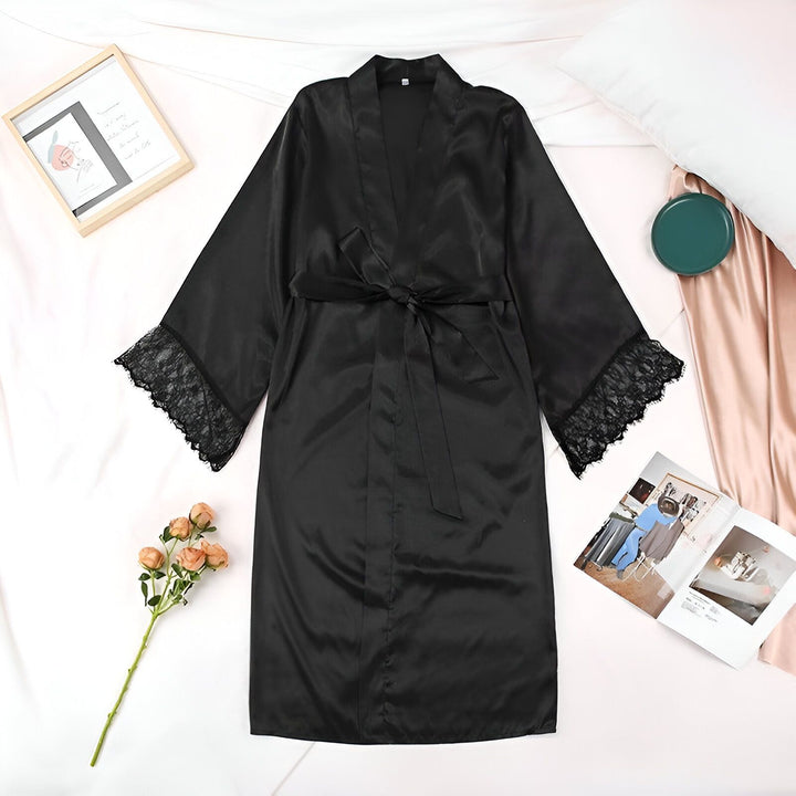 Kimono noir en satin avec manches en dentelle sur un lit. Vêtement de nuit élégant et confortable, idéal pour se détendre à la maison. Parfait comme cadeau ou pour se faire plaisir. Découvrez notre collection de kimonos.